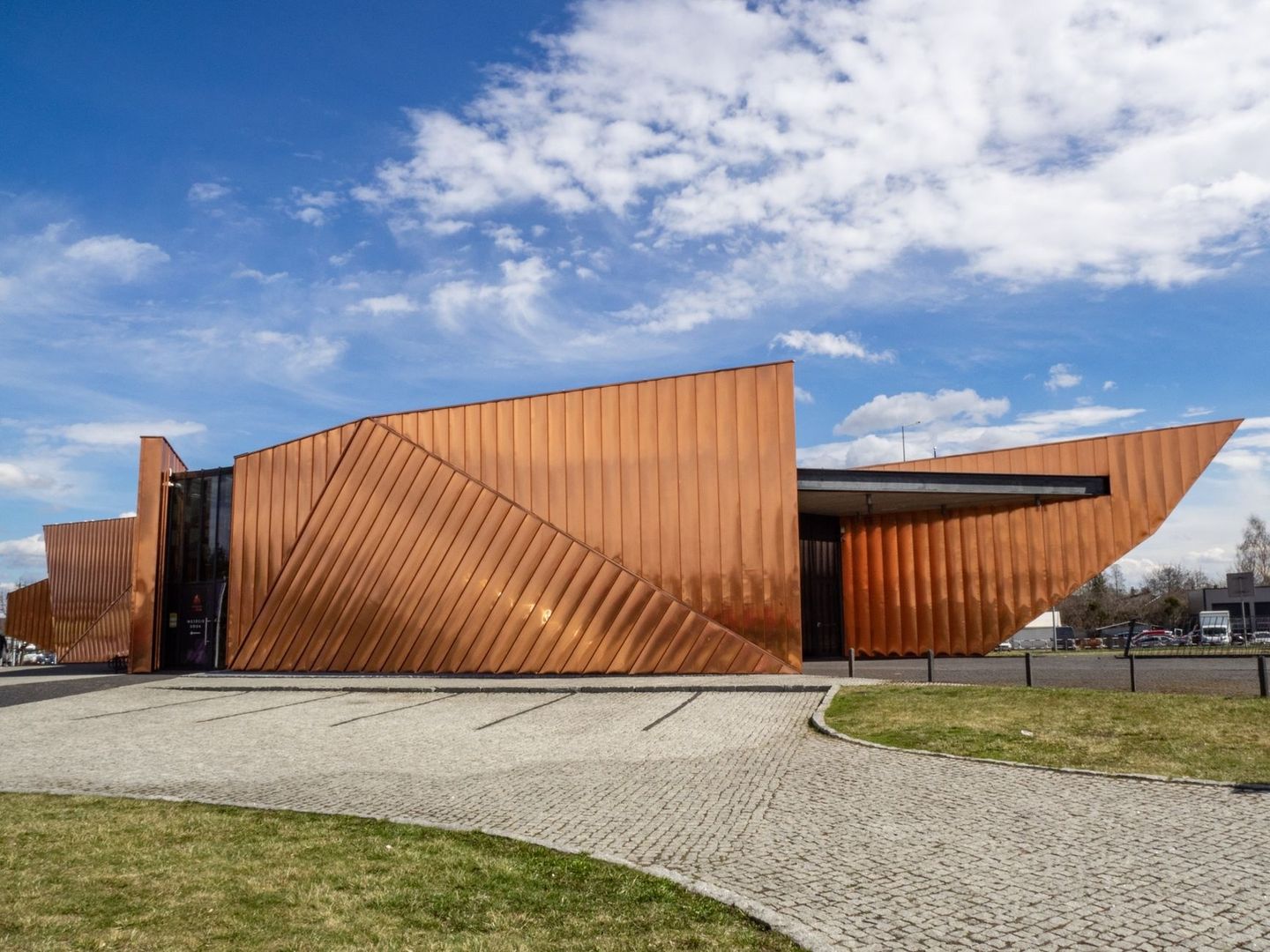 Bâtiment culturel cuivré aux formes anguleuses sous un ciel bleu